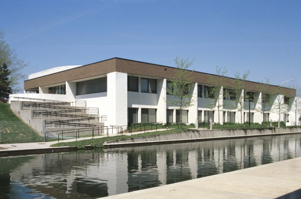 View of the exterior of a two story commercial building with a canal in front of it. 