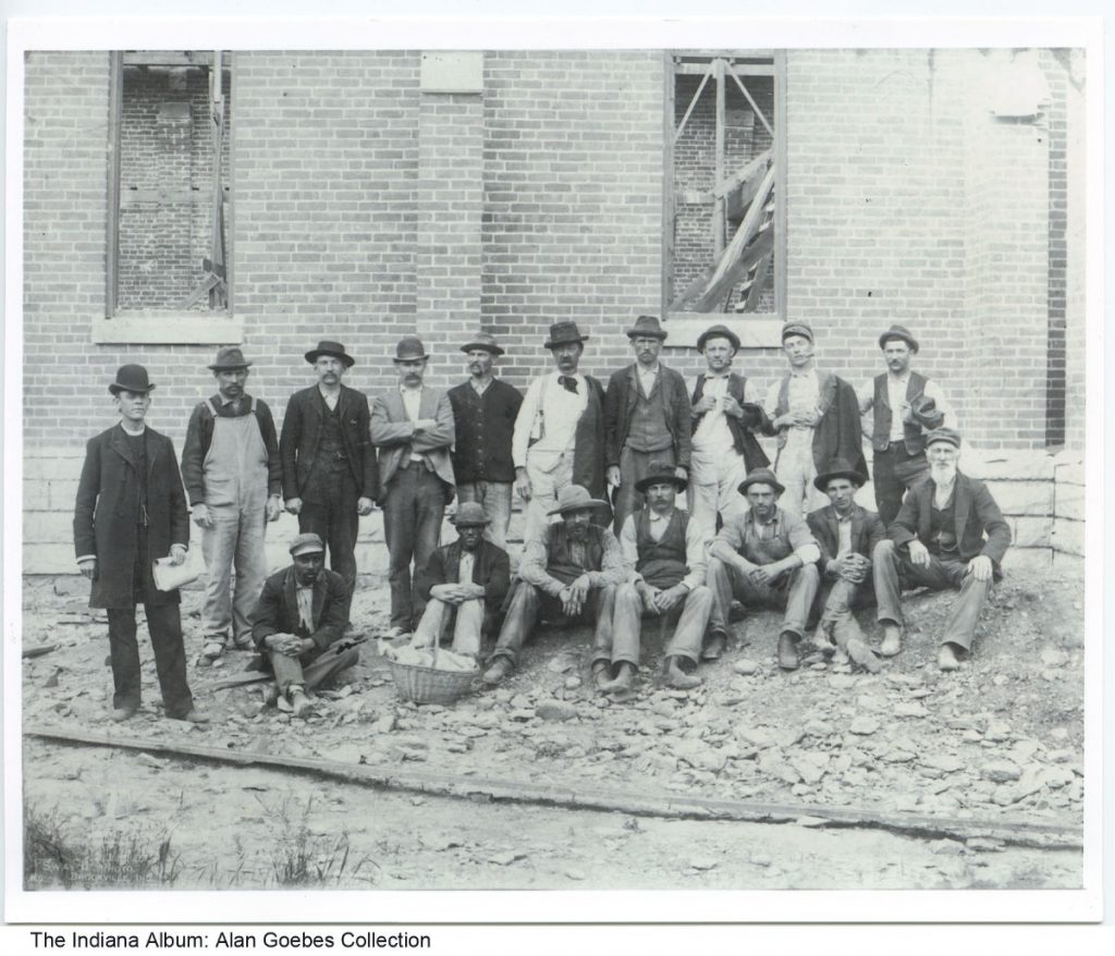 A group of men stand in front of a partially constructed building. 