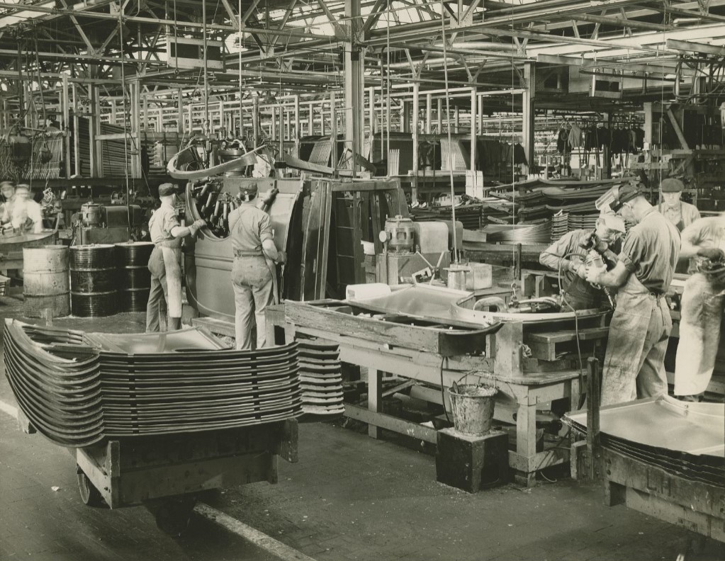 This interior image of the Indianapolis General Motors stamping plant shows several workers taking stamped parts and assembling them. 