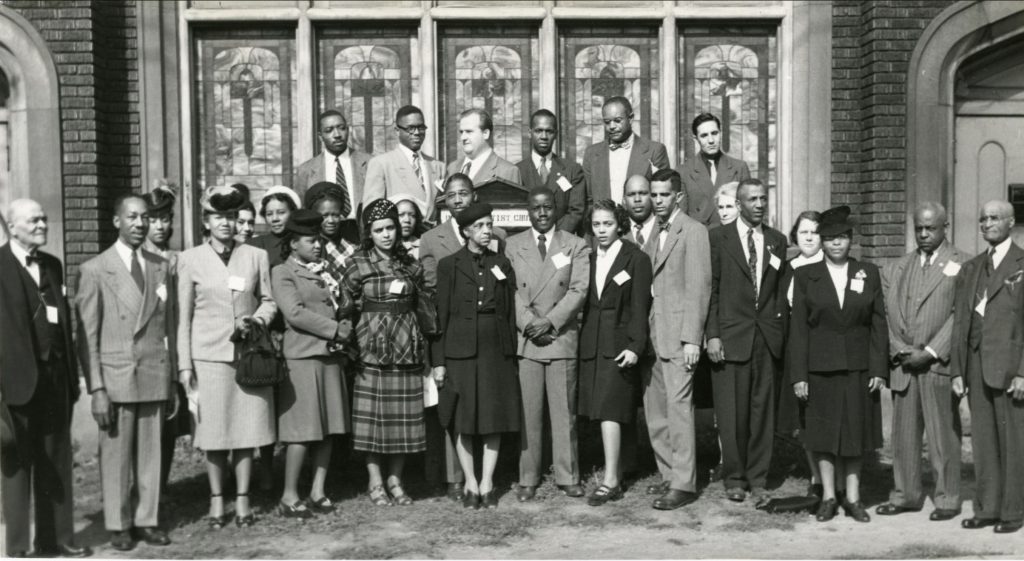 A group of Black citizens stand together for a photo in front of a church building.