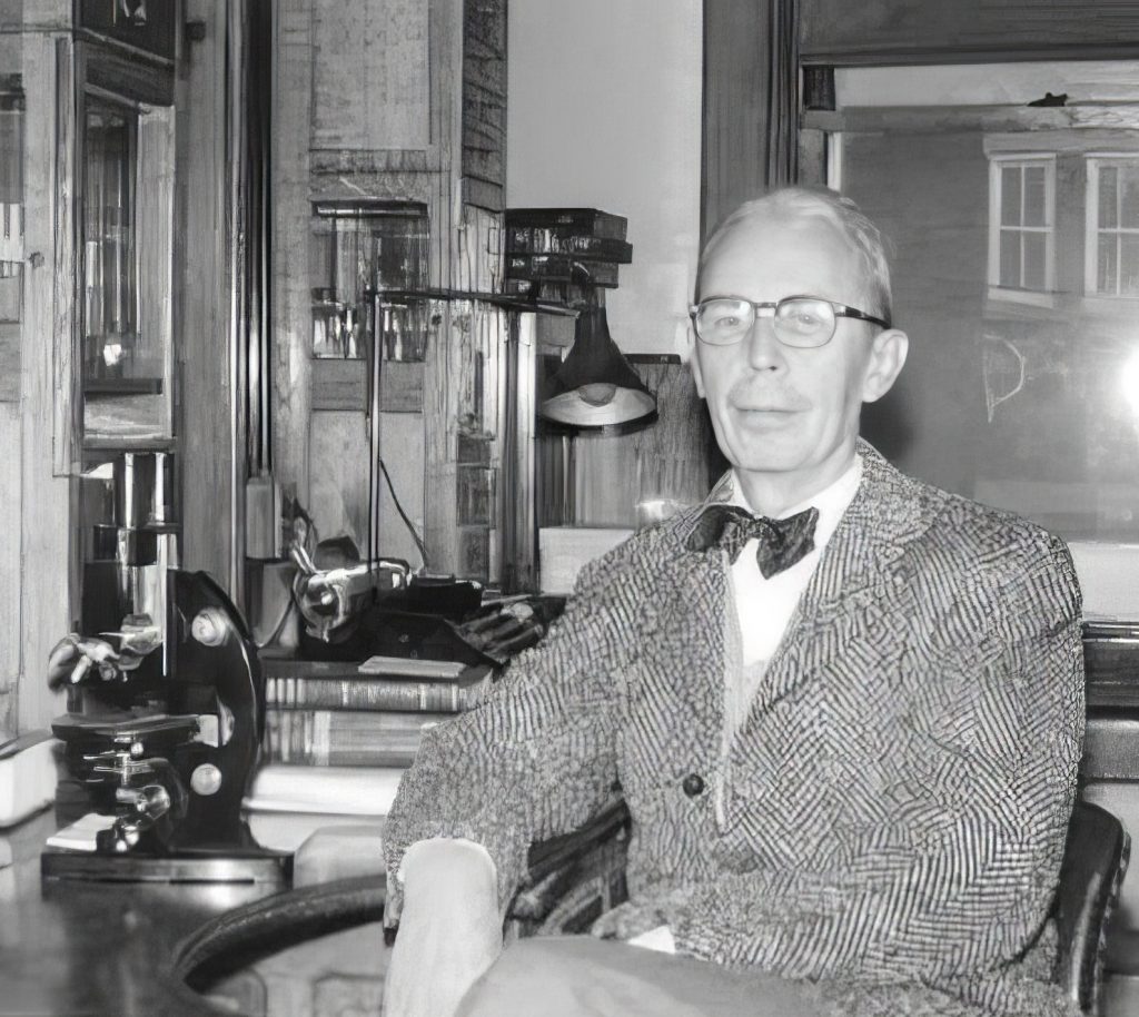 Walter L. Bruetsch sits at a desk with a microscope.