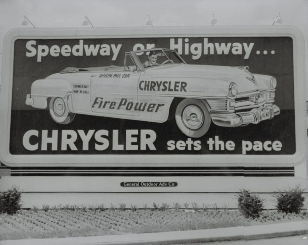 A billboard shows a man in a convertible, which is an "Official Pace Car" and the words "Speedway or Highway...Chrysler sets the pace".