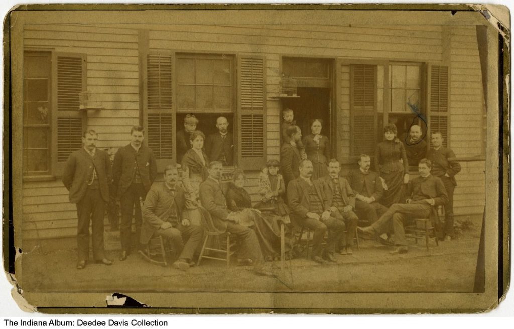 Group of people in front of frame building with shutters. 