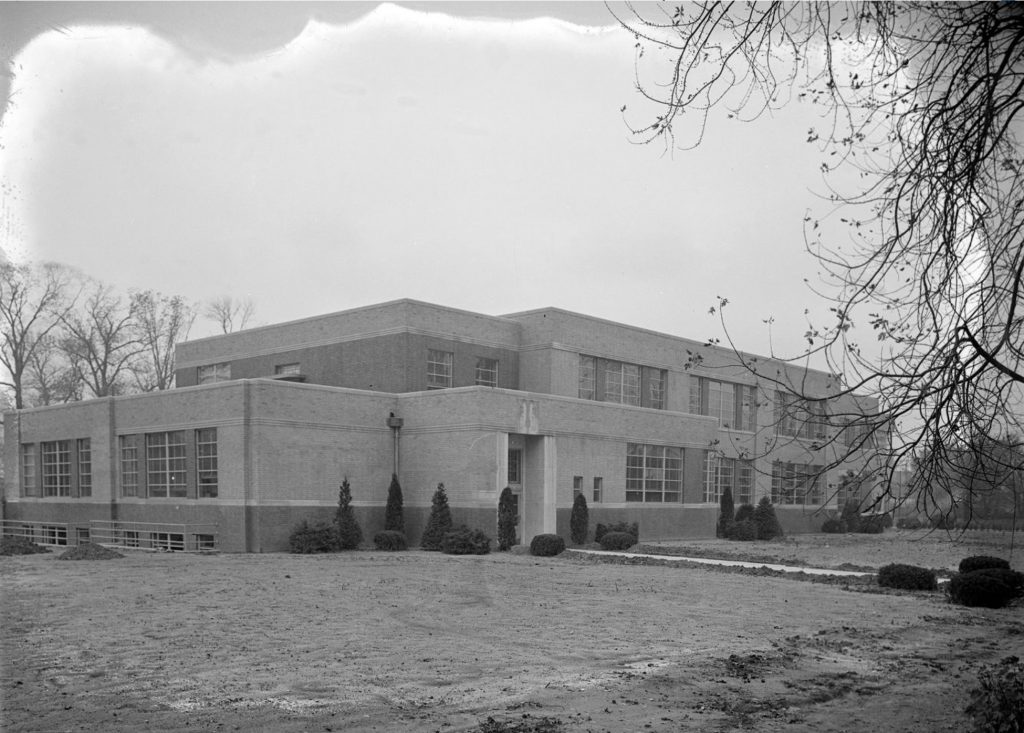 Exterior view of a two-story school building. The Art Moderne style building has a flat roof and horizontal bands of large windows.  