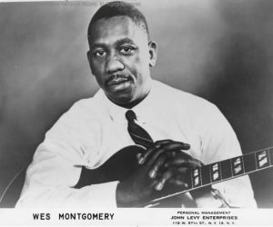 Portrait of Wes Montgomery with his hands resting on a guitar.