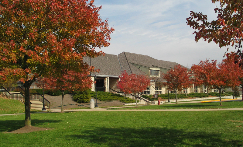 A view of the school building with a green lawn and trees that are changing to fall colors.