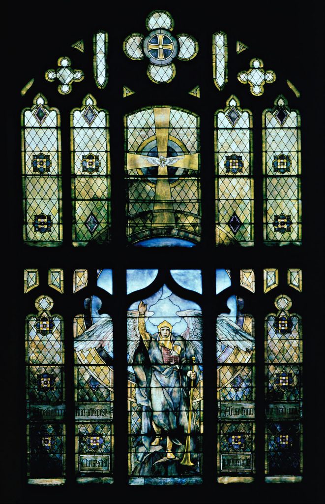 A large stained glass window. The glass depicts an angel with a hand raised up. 