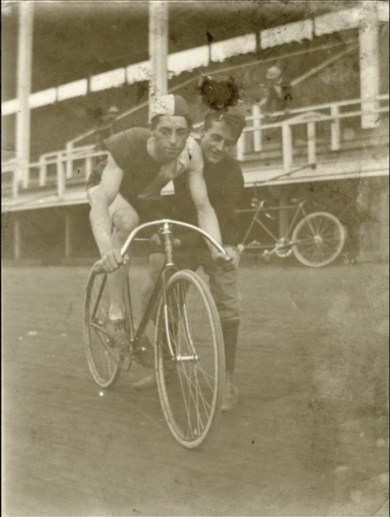 A bicyclist sits on his bike as another man holds the bike up. 