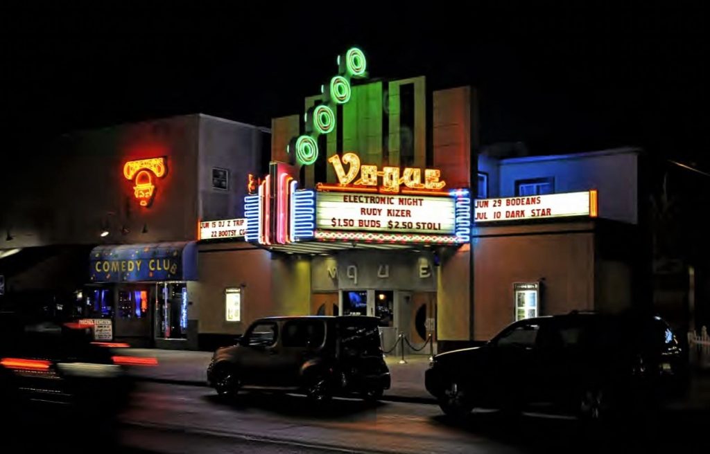 A night view of the entrance of the Vogue. The marquee is lit up with colorful neon lights.