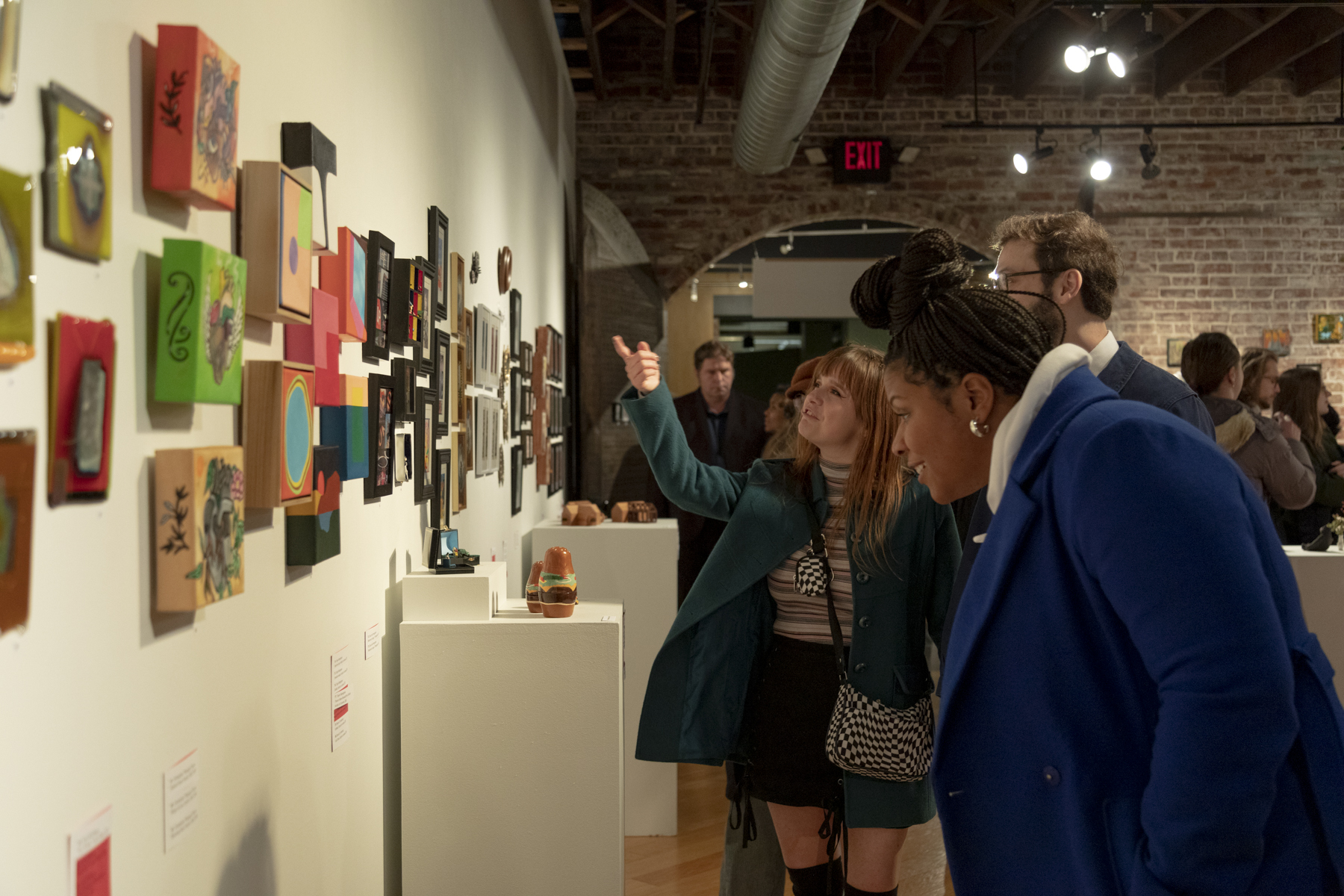 People observe the wall filled with small paintings.