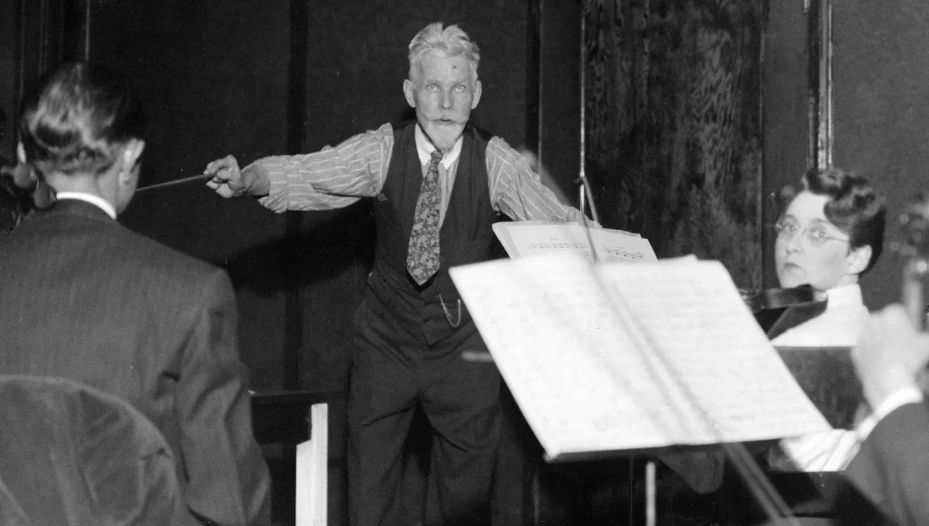 Ferdinand Schaefer actively conducts the musicians seated around him.