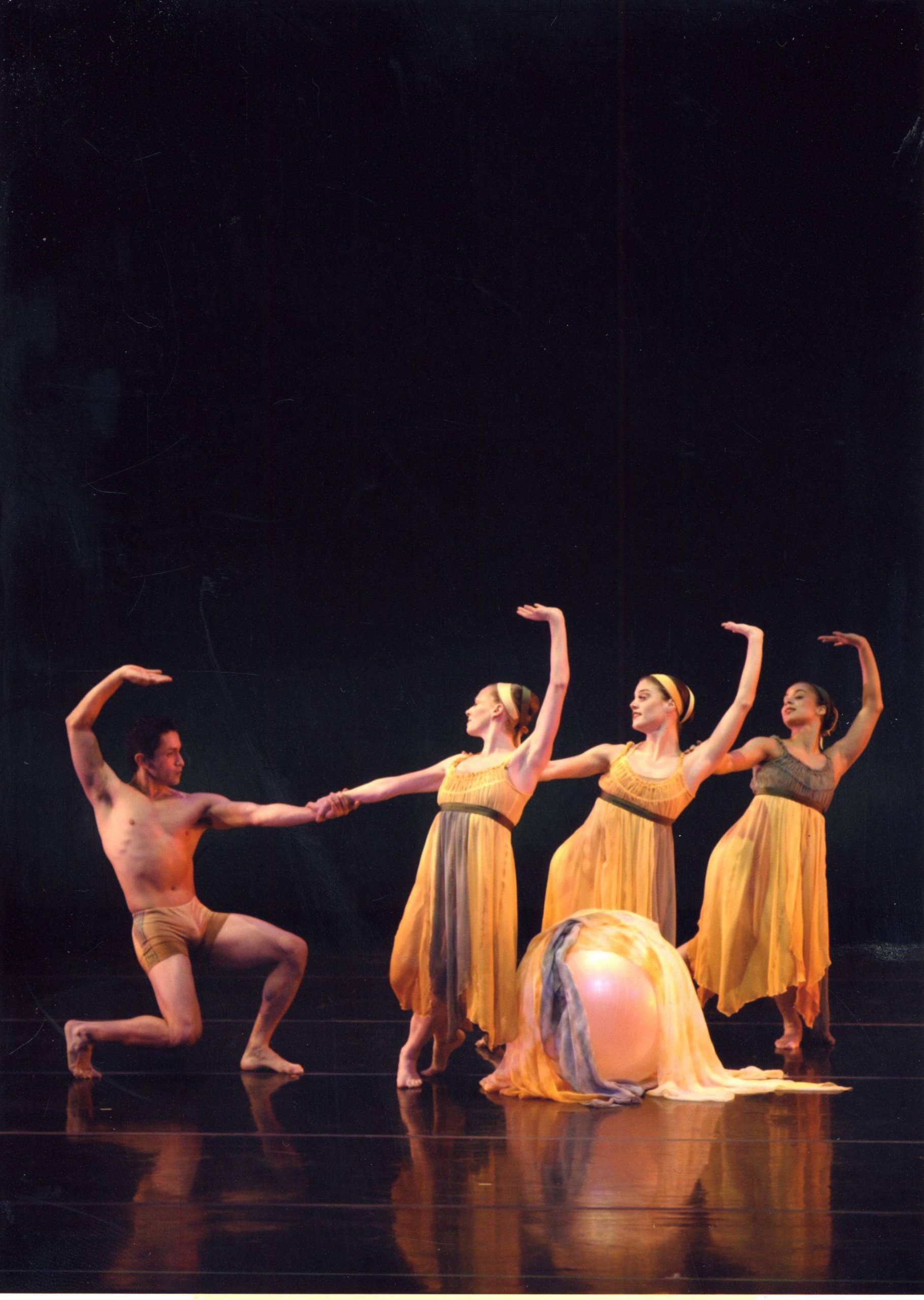A male dancer holds the hand of a female dancer with two dancers behind her.