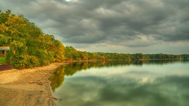 View of a reservoir showing water bounded by a short rocky beach and trees.