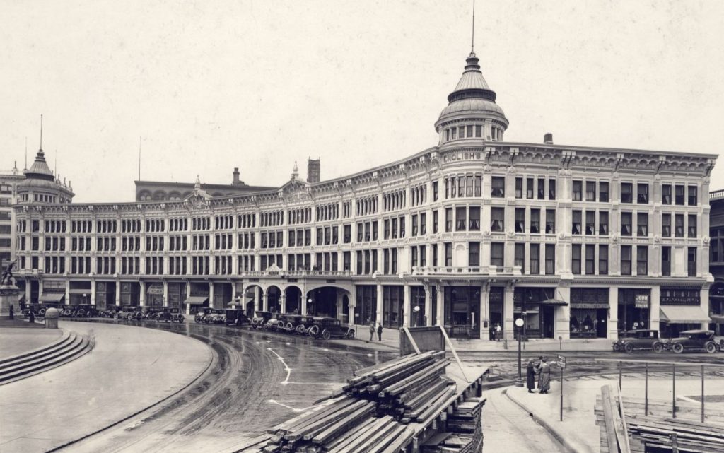 Exterior view of English hotel and opera house in the 1920s with a row of cars parked in front of the building.