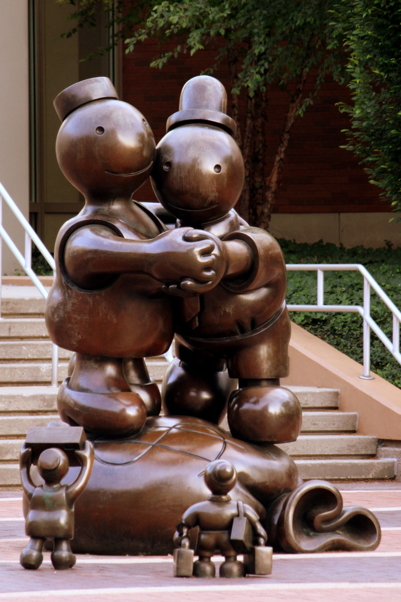 The bronze statue features two human-like figures dancing on a bag with a money symbol on it. Two smaller bronze figures holding suitcases look in the direction of the couple.