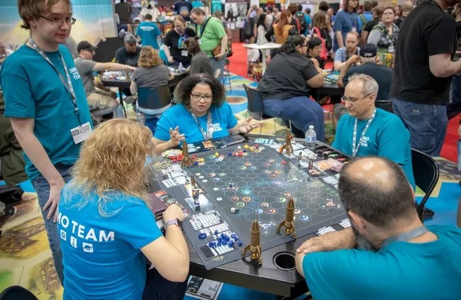 Five people sit around a table playing a board game.