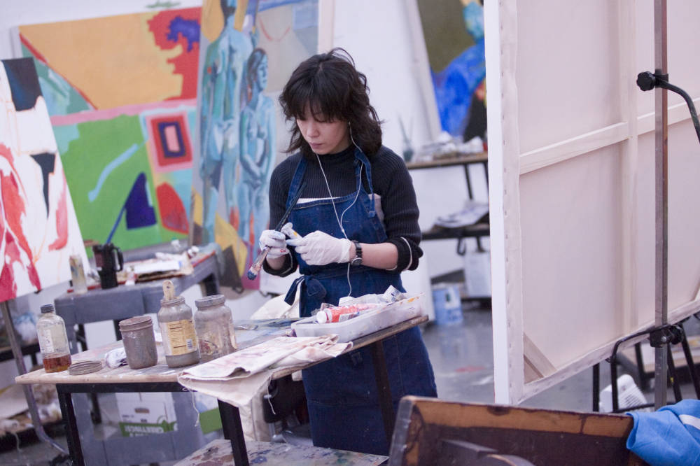 Student in painting class in Herron. She is holding a paint brush and tube of paint.