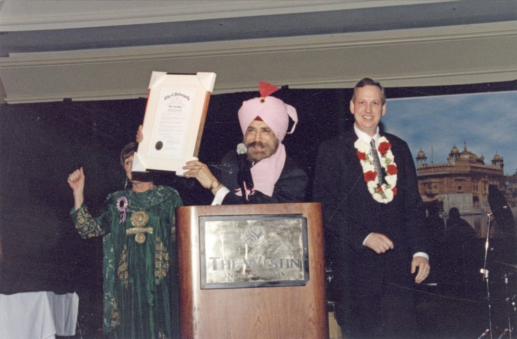 K.P. Singh is on a stage and holding up an award. Bart Peterson is standing next to him.
