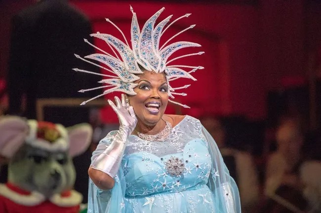 Angela Brown on stage in a blue dress with stars all over it. She also wear silver gloves and a silver headress.
