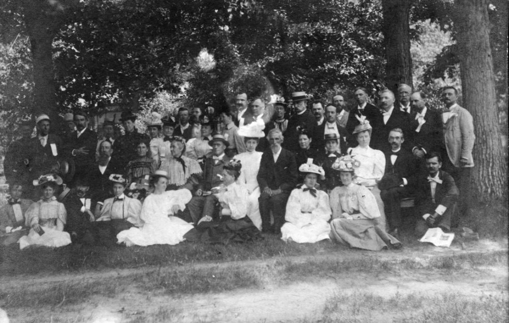 A group of men and women pose for a group photo outside among trees
