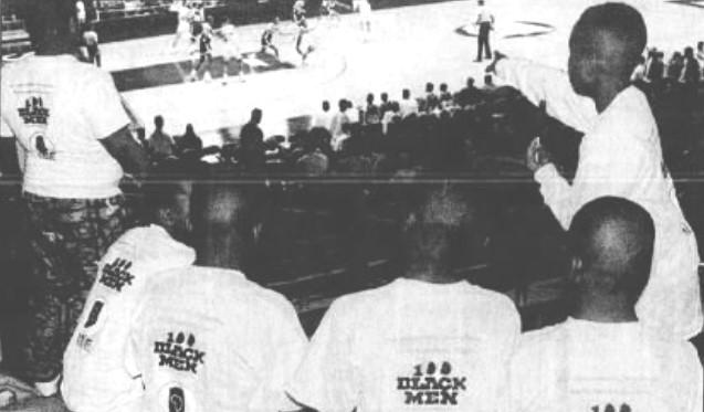 A group of students sit in the stands and watch a basketball game.