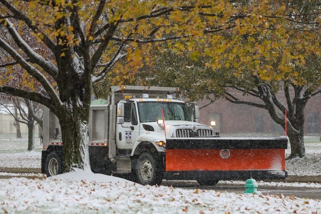 A salt truck with a snow plow on the front drives along a snow-covered street.