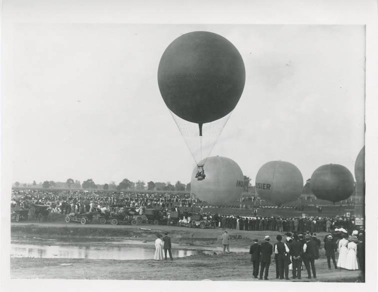 A group of people watch as a hot air balloon is lifted into the air. Three other balloons are aired up, but still grounded.