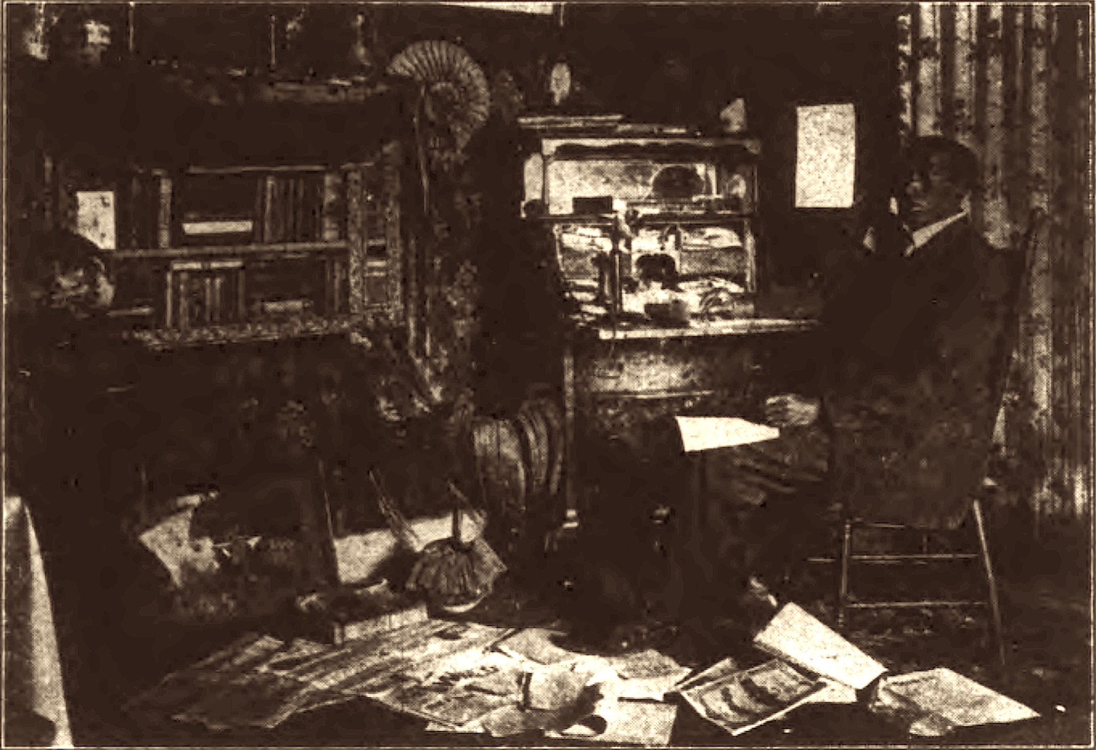 A man sits in a chair at a desk. Papers are strewn about the floor.