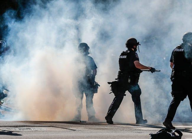 Several police officers stand amid plums of smoke.