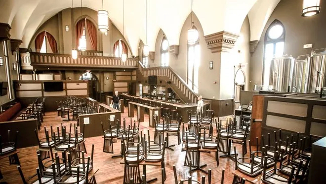 Interior view of a church building that has been adapted to a restaurant. There are many tables and booths in the middle with a bar off to the side. 