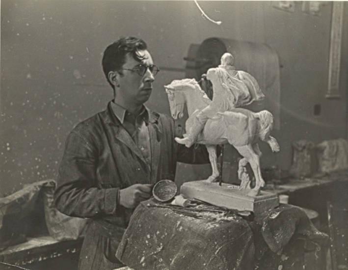 A man works on a small sculpture of a person on a horse.