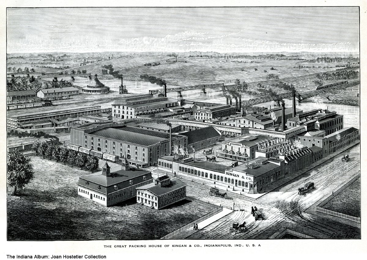 An aerial view of a group of low buildings; many with smokestacks.