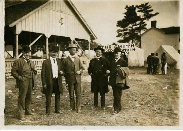 A group of five men stand outside in the fairgrounds.