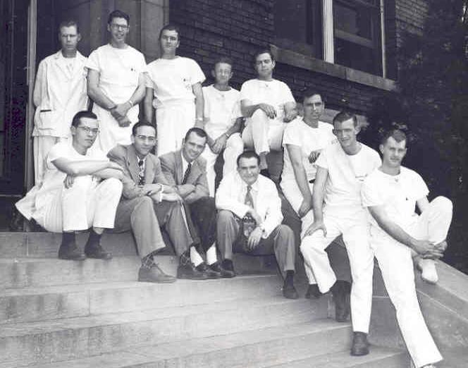 A group of men dressed in all white are sitting on the steps leading into a building.
