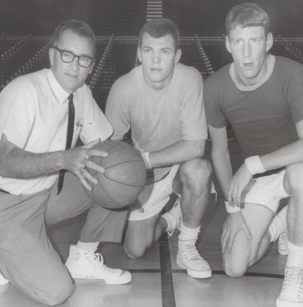 A man kneels while holding a basketball. Two young men kneel next to him.