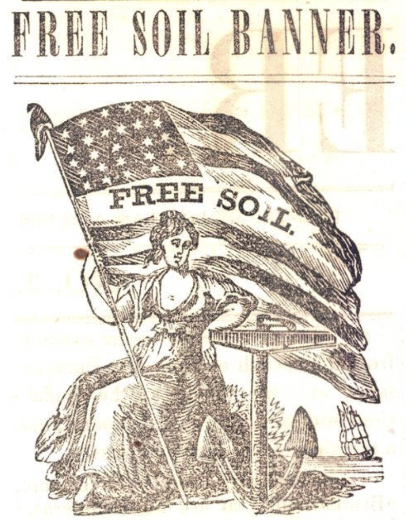 A woman sits at a table holding an American flag which has "Free Soil" printed on it.