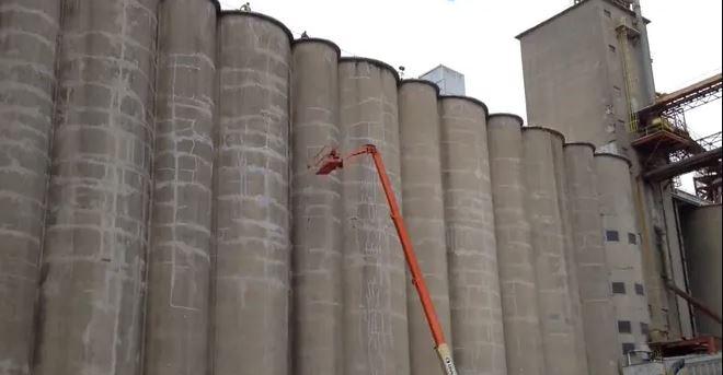 The arm of a bucket truck is extended to the middle part of a series of connected grain bins.