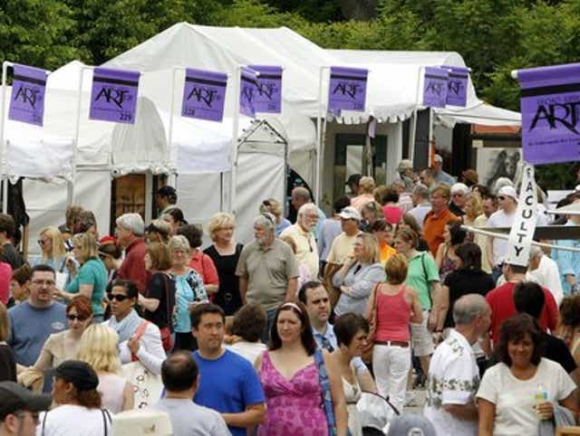 A crowd of people mill around in front of a row of white tents.