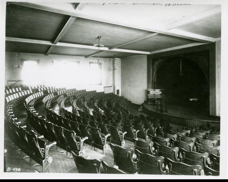 The interior of a large theatre with empty seats arranged in semi-circular rows ascending from the stage.
