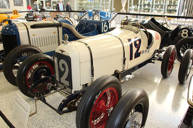 An old-fashioned, perfectly restored race car is displayed with other vintage models.