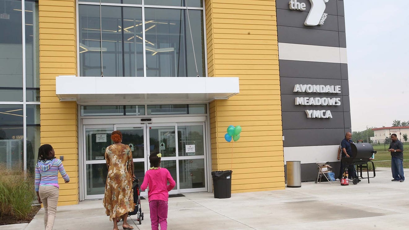 Three people are shown approaching the entrance of a modern building. A sign on the building to the right of the entrance reads "Avondale Meadows YMCA".