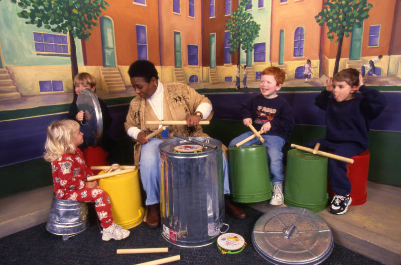 Betty Perry teaches three children how to play music using drum sticks and overturned trashcans.