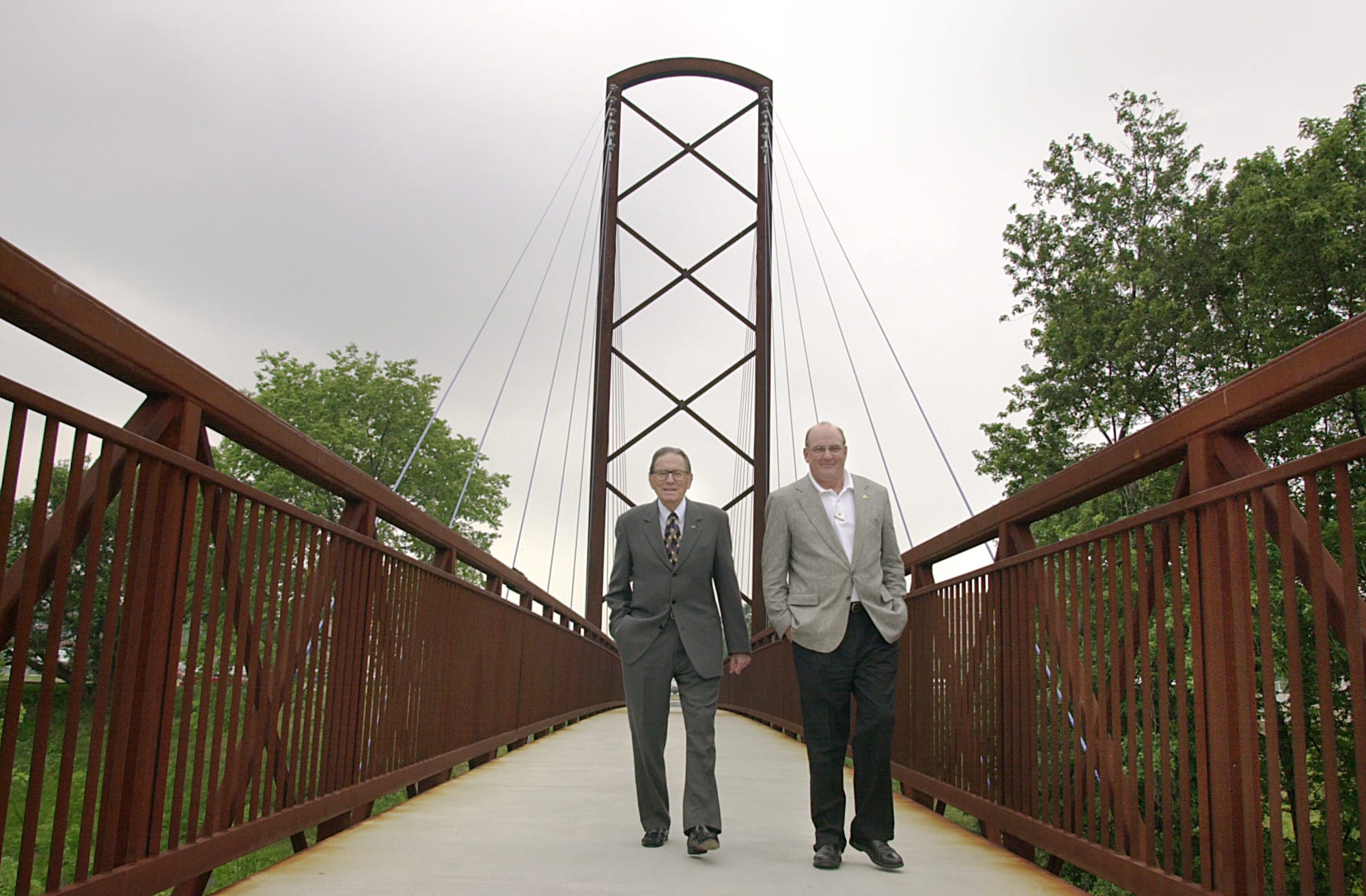 Two men stand on a walking bridge.