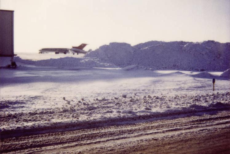 Two jets are parked on a field of snow and snowpiles.
