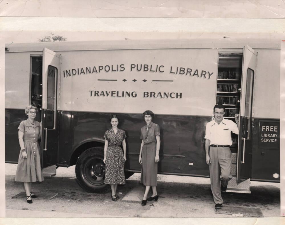 Four people stand in front of a bus with its doors open.