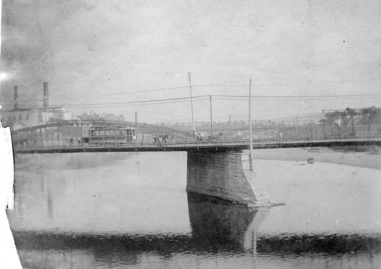 A flat bridge supported by a concrete pier crosses a river.