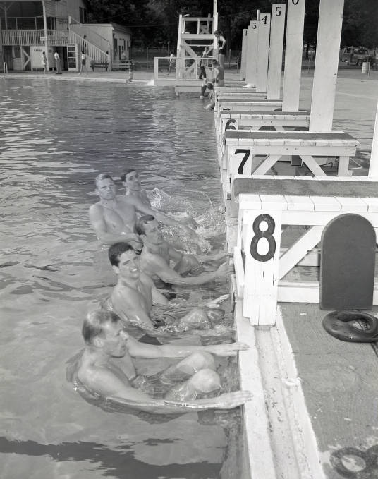 Five men are in the pool and holding onto the side as if about to begin a race.