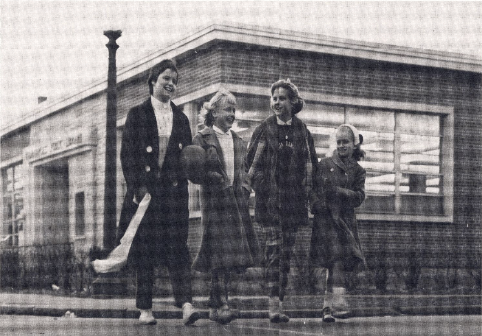 Four people are walking in front of a library building.