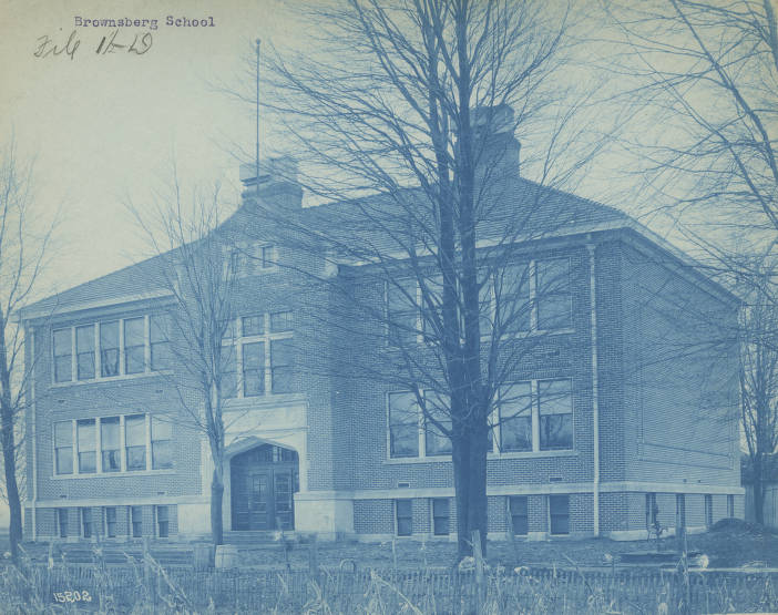 The school is a brick, three-story rectangular building with two chimneys and white stone trim around the entrance.