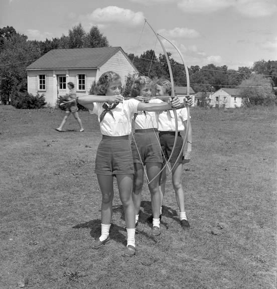 Three girls are on a lawn with cabins in the background.